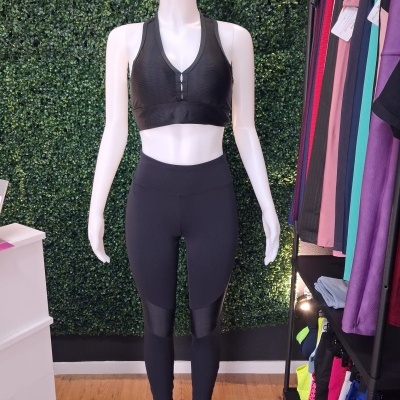 Mannequim com conjunto desportivo preto em fundo de parede verde de folhagem e estante de roupas coloridas
