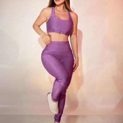 Mulher com conjunto desportivo lilás e sapatilhas brancas num fundo claro