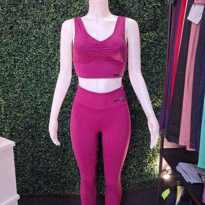 Conjunto desportivo feminino fúcsia em manequim com fundo de folhagem verde