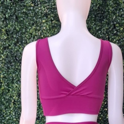 Top desportivo cor de vinho numa maniquim com fundo verde de folhagem