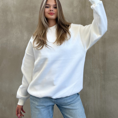 Mulher com sweatshirt branca e jeans azuis claros segurando mala preta com padrão monograma