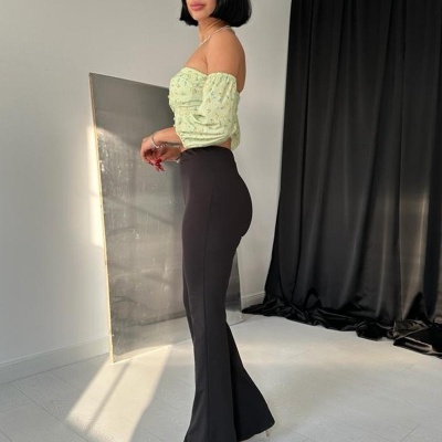 Mulher com blusa verde clara e calças pretas em ambiente interior com cortinas pretas