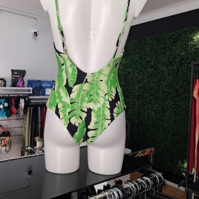 Fato de banho verde com padrão de folhas em manequim branco visto de costas numa loja de roupa.