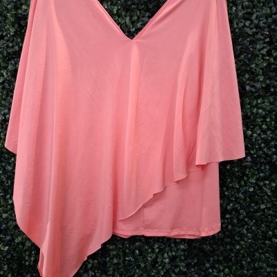 Poncho ou capa rosa claro com decote em V numa cabide preta com fundo verde