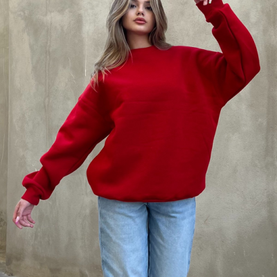 Mulher com sweatshirt vermelha e jeans azul claro em fundo de parede bege