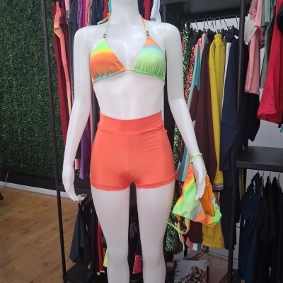 Maniquim branco com biquíni colorido e shorts laranja em loja de roupa