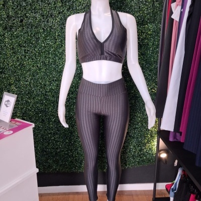 Conjunto desportivo feminino cinza escuro em manequim branco com fundo de folhagem artificial