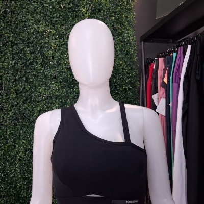 Top desportivo preto de alças assimétricas num manequim contra fundo verde e roupas coloridas ao lado