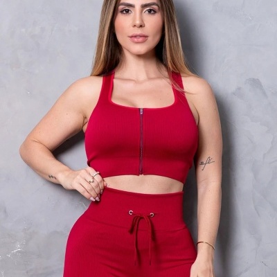 Conjunto desportivo vermelho de mulher com top e leggings, fundo cinza.