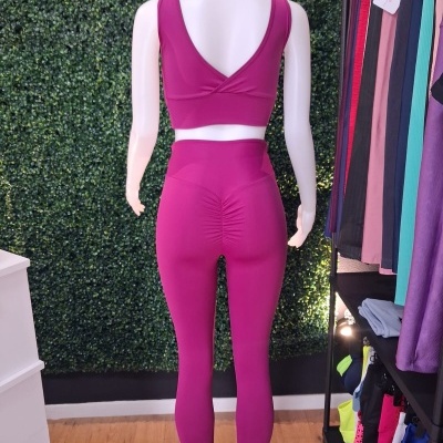 Manequim com conjunto desportivo cor de rosa com top e leggings, de costas, em loja com parede verde e roupas coloridas à direita.