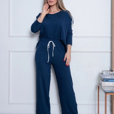 Mulher com conjunto azul escuro de calças e camisa de mangas compridas em ambiente interior branco