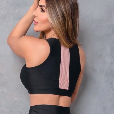 Top desportivo preto com detalhe rosa e leggings pretas numa mulher de costas contra parede cinzenta