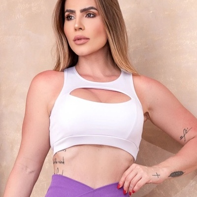 Mulher com top desportivo branco e calças justas roxas num fundo bege.