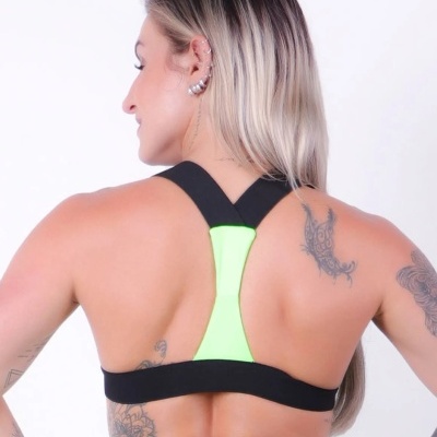 Top desportivo preto com detalhe verde fluorescente nas costas, visto por mulher com tatuagens