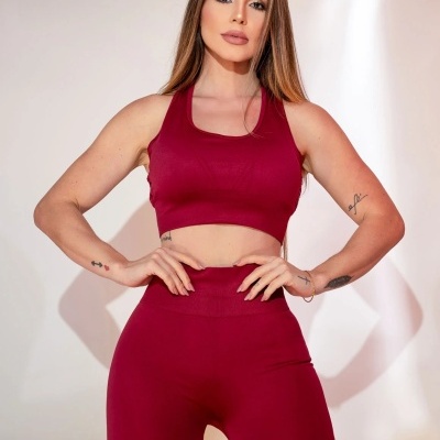 Mulher vestindo conjunto de desporto bordô, top e leggings, fundo branco