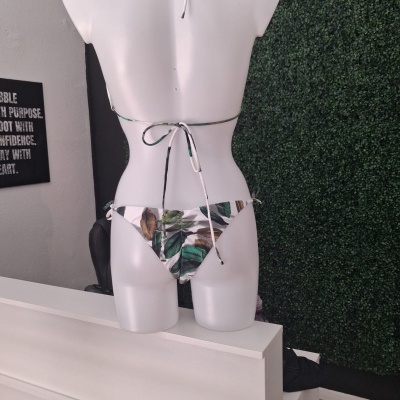 Biquíni com padrão de folhas num manequim branco em loja com parede verde