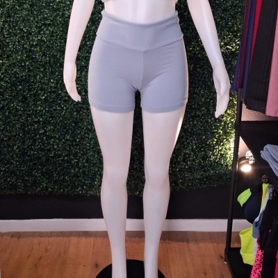 Mannequim com calções curtos cinzentos em ambiente interior com parede verde e prateleira de roupas ao lado