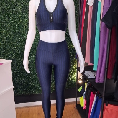 Conjunto desportivo azul escuro em manequim com parede verde e roupas coloridas ao lado.