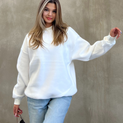 Mulher com camisola branca e calças de ganga azuis junto a parede cinza