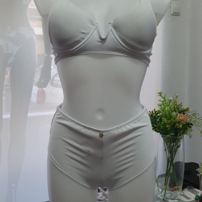 Conjunto de lingerie branco canelado em manequim com mesa de vidro e planta ao lado.