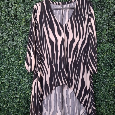 Blusa comprida com padrão zebra em cabide contra fundo de folhagem verde