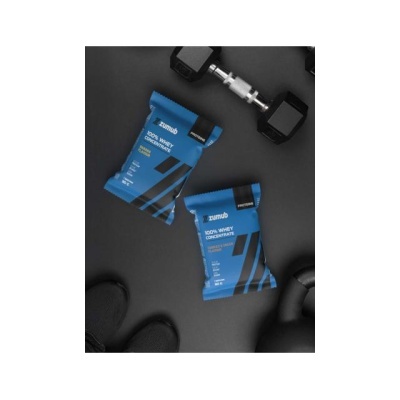 Duas embalagens azuis de suplemento proteico Zumub 100% Whey Concentrate junto a equipamento de ginásio preto.