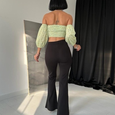 Mulher com top verde e calças pretas numa sala com cortina preta.