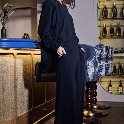 Mulher com conjunto preto e brincos grandes em bar com banquetas azuis