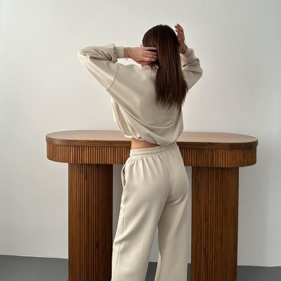 Mulher de costas com conjunto desportivo bege e ténis junto a mesa de madeira