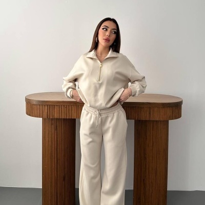 Mulher a usar conjunto bege de sweat e calças largas junto a mesa de madeira