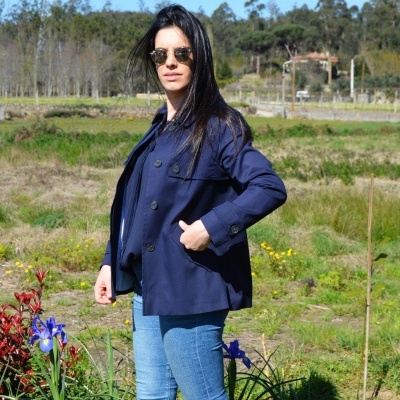 Mulher com casaco azul escuro e óculos de sol num campo verde com flores