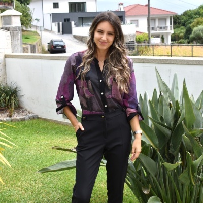 Mulher com camisa colorida e calças pretas num jardim