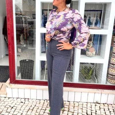 Mulher com blusa floral, calças cinza e sapatos verdes na rua frente a montra.