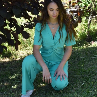 Mulher ajoelhada em relvado com macacão verde água de manga curta e calças largas