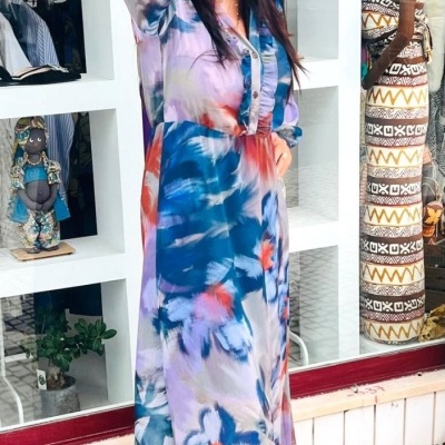 Mulher com vestido longo colorido e chapéu vermelho em frente a montra com estatuetas africanas