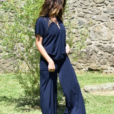 Macacão azul escuro em tecido fluido usado em jardim com parede de pedra