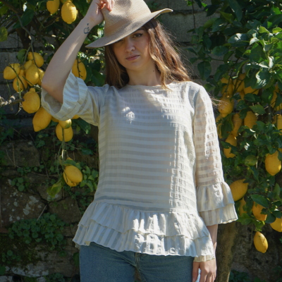 Blusa branca com riscas e folhos, mulher com chapéu bege junto a árvore de limão