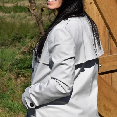 Mulher com casaco bege claro, jeans azul e óculos de sol junto a porta de madeira ao ar livre