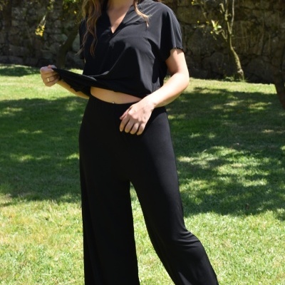 Mulher com conjunto preto de top e calças largas em jardim verde