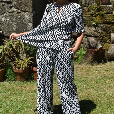 Conjunto feminino preto e branco com padrão abstracto num jardim, mulher com óculos escuros e sapatos castanhos