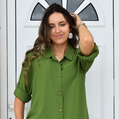 Camisa verde de manga curta com botões sendo usada por mulher diante de porta branca