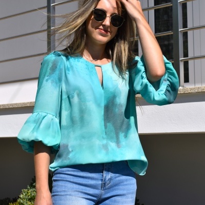 Mulher com blusa azul clara e calças de ganga azuis ao sol junto a parede branca