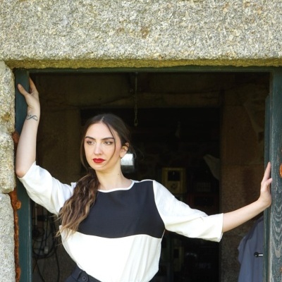 Mulher com blusa bicolor preta e branca e calças pretas numa porta de pedra