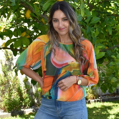 Mulher com blusa colorida abstrata e calças jeans num jardim