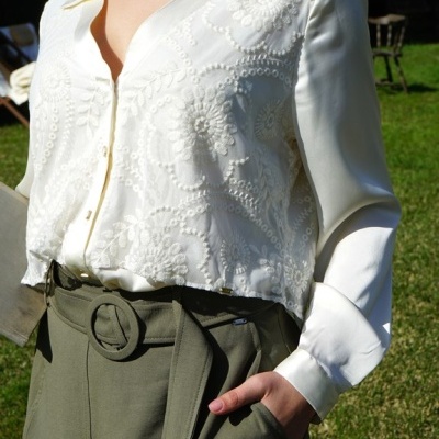 Blusa branca feminina com padrões florais e saia verde-oliva com cinto ao ar livre