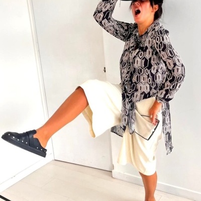 Mulher com roupa estampada e chapéu preto segura carteira em ambiente claro