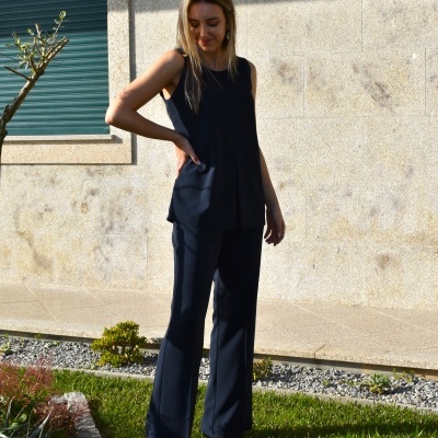 Conjunto feminino azul escuro sem mangas e calças largas num jardim junto a parede de pedra clara.