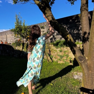 Vestido comprido azul e verde com padrão de círculos, em jardim ao sol