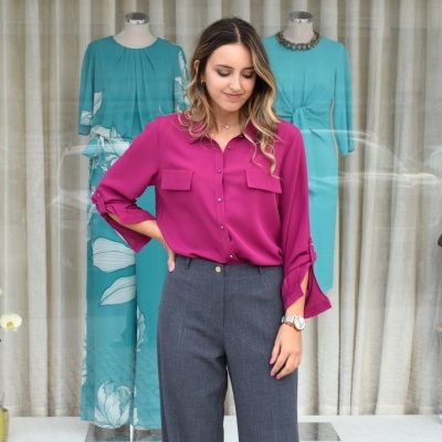 Mulher com camisa fúcsia e calças cinza em frente a montra com manequins vestidos de azul turquesa