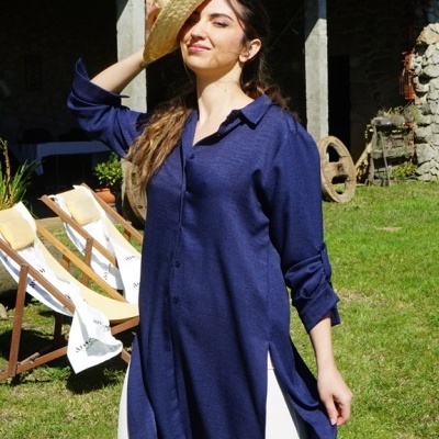 Mulher com camisa azul escura e calças brancas segurando chapéu de palha ao ar livre